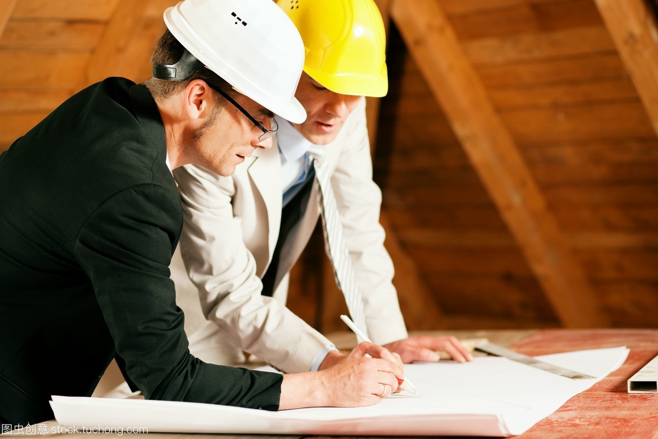 建筑師和建筑工程師或測量師的討論計劃和藍圖。兩人都戴著安全帽,站在一個室內的建筑工地